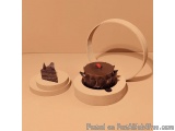The image shows two small cakes on a white surface. The cake on the left is a slice of chocolate cake with a red cherry on to...