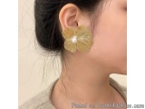 The image shows a close-up of a woman's ear. She is wearing a pair of gold earrings in the shape of a flower. The earrings ha...
