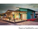 The image shows a small, single-story house with a green exterior and a wooden roof. The house is located on a street with a...