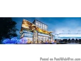 The image is a digital rendering of a modern building at night. The building is a two-story structure with a curved roof and...