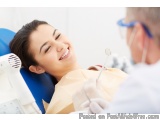 The image shows a young woman sitting in a dental chair with her mouth open and a big smile on her face. She is wearing a bei...