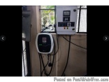 The image shows an electric vehicle charging station. The station is mounted on a wall with a window in the background. On th...