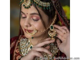 The image is a close-up portrait of a young Indian woman wearing traditional Indian jewelry. She is wearing a red and gold le...
