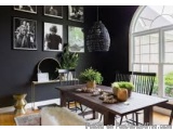 The image shows a dining room with a large window on the right side. The walls are painted black and there are several framed...