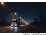 The image shows a long, straight road at night. The road is empty and the sky is dark, indicating that it is nighttime. On th...