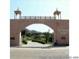 The image shows the entrance of Raj Mahal Resort. The entrance is made of stone and has a large archway with two small towers...