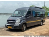 The image shows a black van parked on a sandy beach next to the ocean. The van has a yellow stripe running along the side and...