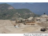 The image shows a large open-pit mine with a mountain range in the background. The mine appears to be in the process of being...