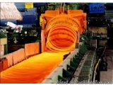 The image shows a large orange-colored machine in a factory. The machine appears to be a conveyor belt or a hopper, with mult...