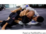 The image shows two men engaged in a Brazilian Jiu-Jitsu (BJJ) fight. The man on the left is wearing a black jiu-jitsu suit a...
