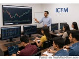 The image shows a group of people sitting at desks in front of multiple computer monitors in a trading room. The room has a w...