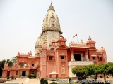 The image shows a large, ornate temple with a tall, white dome on top. The temple is made of stone and has multiple levels wi...