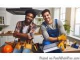 The image shows two young men in a kitchen, both wearing overalls and smiling at the camera. They are standing in front of a...