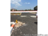 The image shows an empty parking lot with a white fence surrounding it. The parking lot is empty and there is a yellow bollar...
