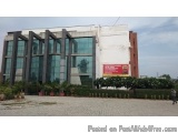 The image shows a modern building with a glass facade. The building is located in a residential area with a clear blue sky in...