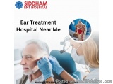 The image shows a man sitting in a dental chair with a dentist examining his ear. The dentist is wearing a blue glove and is...