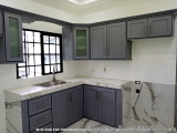 The image shows a modern kitchen with a large island in the center. The island has a white countertop with a sink and a windo...