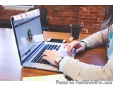 The image shows a person sitting at a wooden desk with a laptop in front of them. The laptop is open and the screen is displa...
