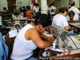 The image shows a group of people working in a sewing factory. There are several sewing machines and workers in the backgroun...