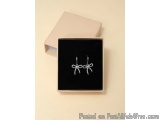 The image shows a small rectangular box with a black velvet lining. Inside the box, there is a pair of silver earrings. The e...