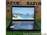 The image shows a black laptop computer sitting on a green grassy surface. The laptop is open and the screen is turned on, di...
