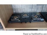 The image shows a black gas stove with three burners on top of it. The stove has four burners with gold-colored knobs for adj...