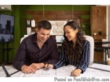 The image shows a young couple sitting at a desk in an office. The man is on the left side of the image, wearing a black shir...