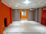 The image shows an empty room with a white tiled floor and orange walls. The room has a high ceiling with recessed lighting a...
