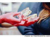 The image shows a person's hand wearing a red glove holding a model of a human jaw. The model appears to be made of plastic a...