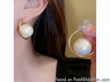 The image shows a close-up of a person's ear. The person is wearing a pair of gold hoop earrings with a white pearl in the ce...
